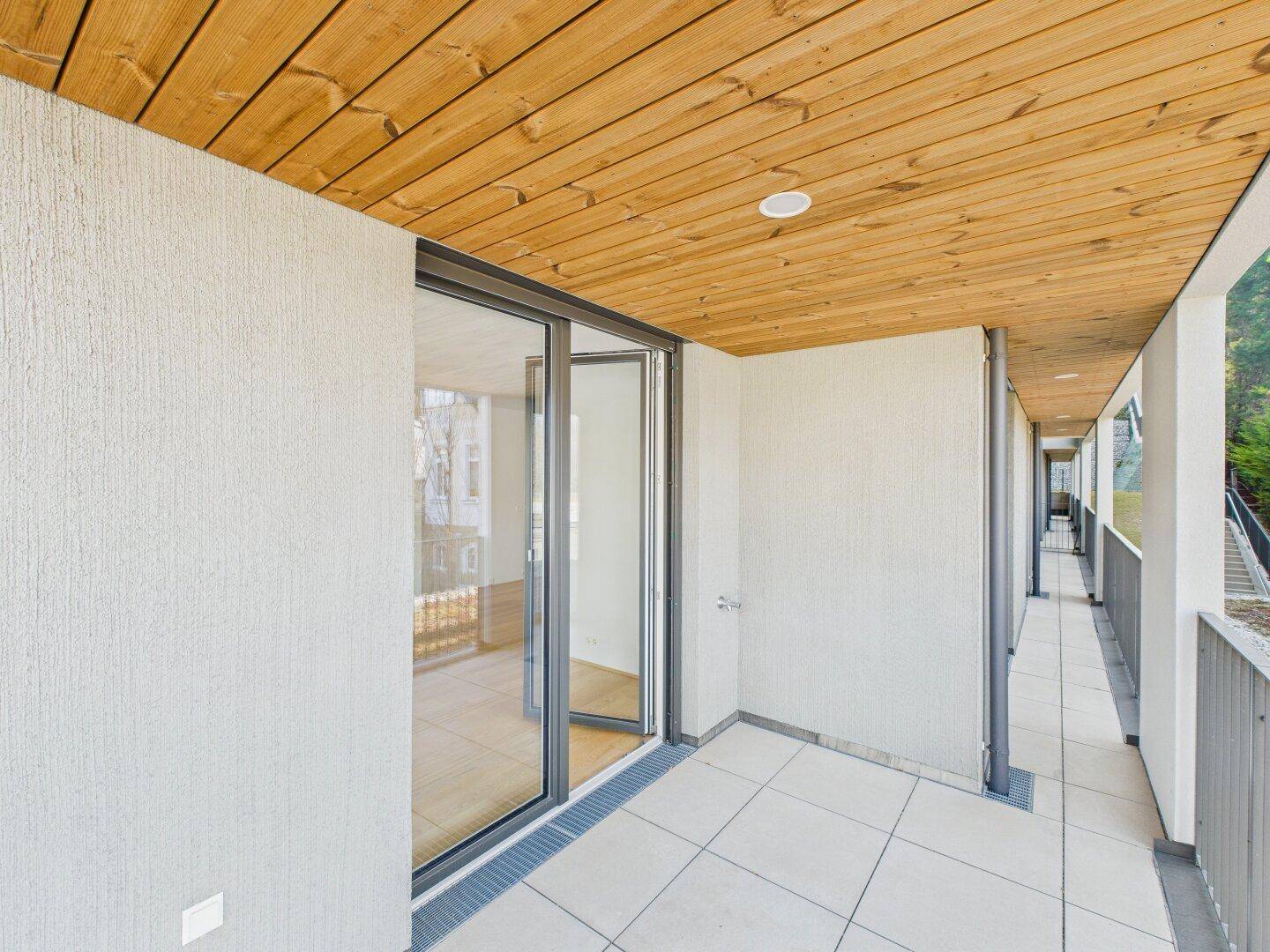 Langer, überdachter Balkon mit Fliesenboden und Holzdach, ideal für entspannte Stunden im Freien.