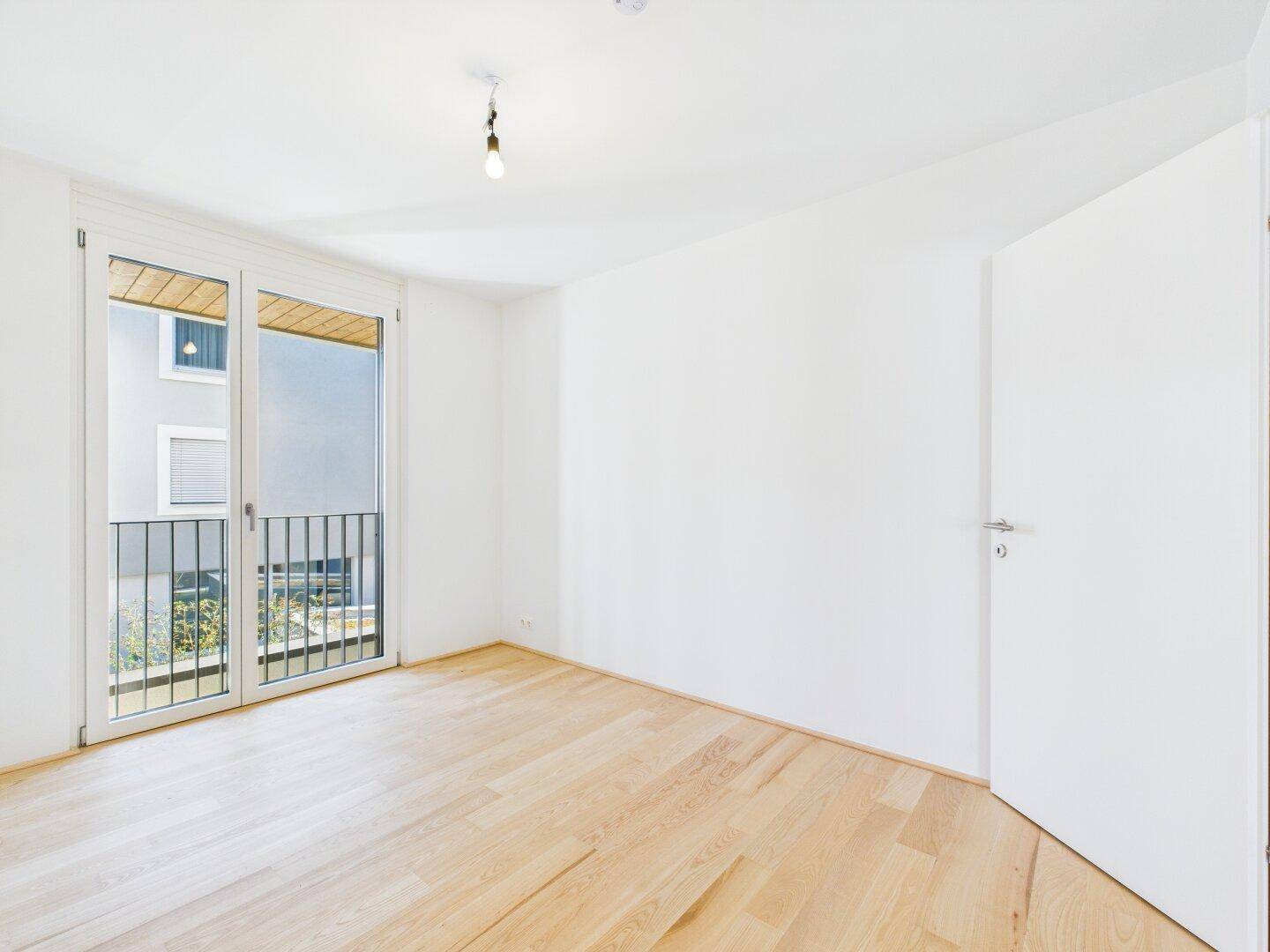 Helles Zimmer mit Holzboden und Balkonzugang, bietet viel Tageslicht und frische Luft.