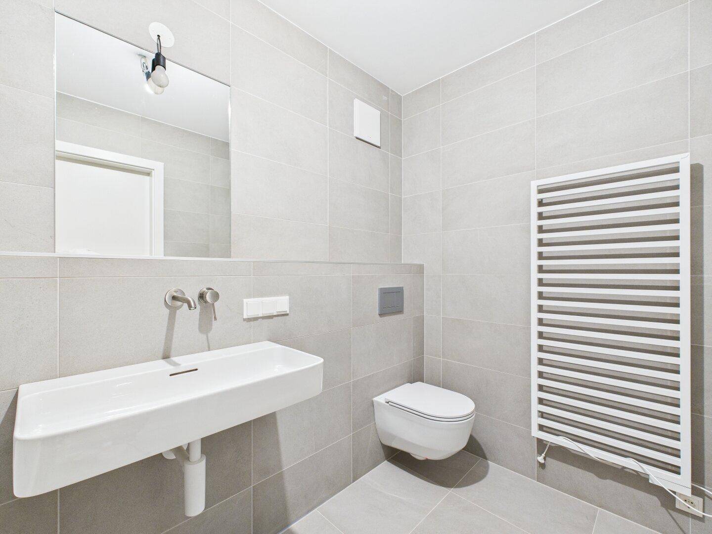 Modernes Badezimmer mit wandhängendem WC, Waschbecken, Spiegel und Handtuchheizkörper.