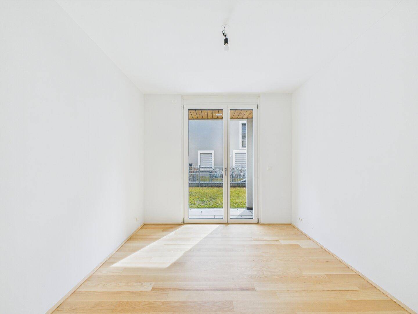Sonnendurchflutetes Zimmer mit Parkettboden und großen Fenstern, die viel Licht spenden.