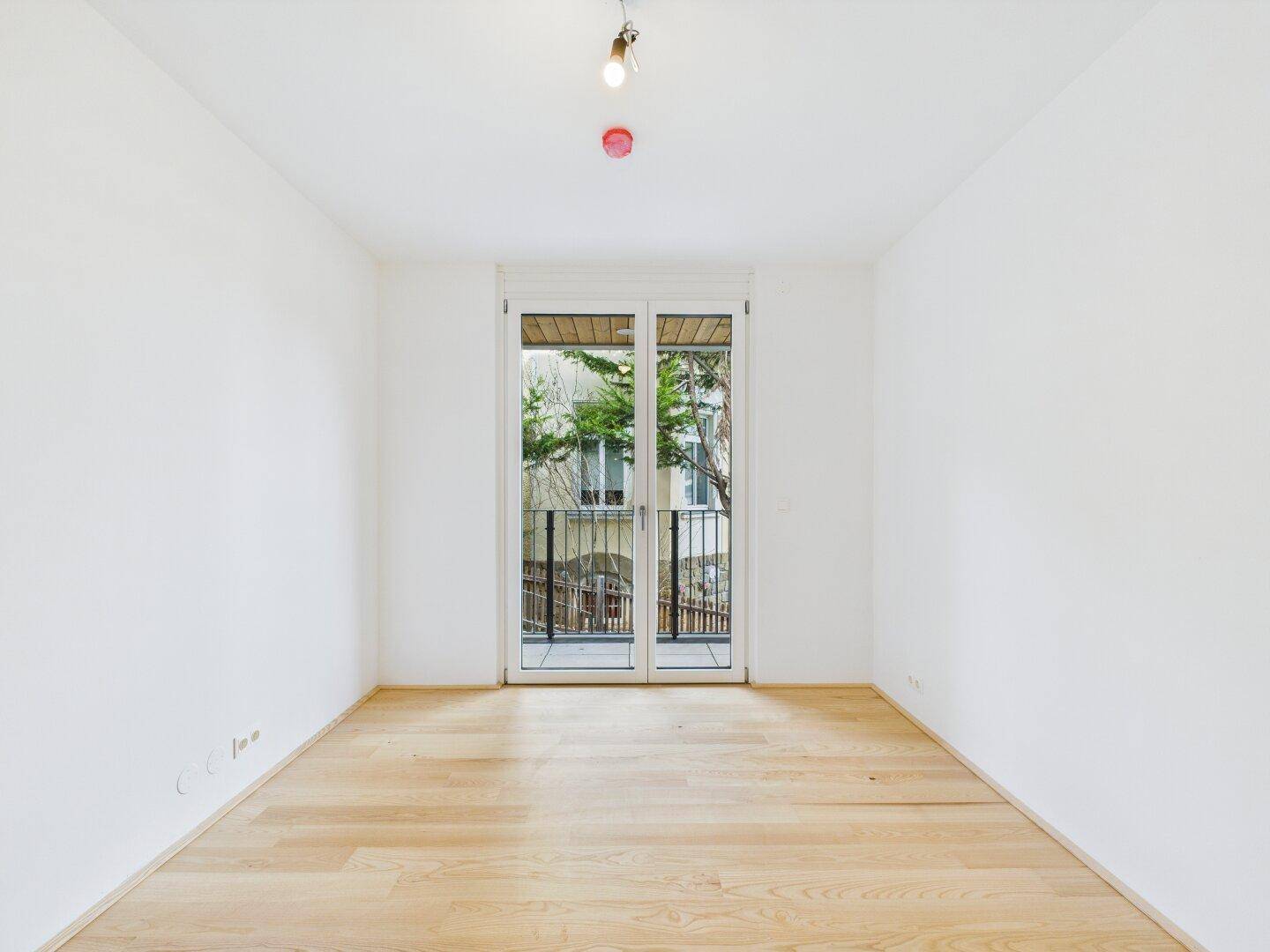 Sonniges Schlafzimmer mit hellem Parkettboden und Zugang zu einem kleinen Balkon.