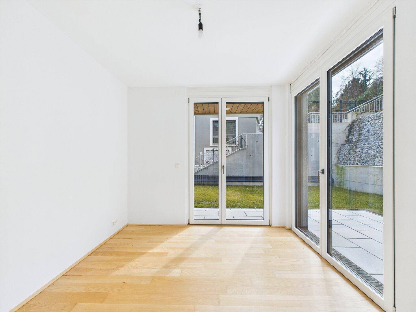 Helles Zimmer mit Parkettboden und großen Fenstern, die einen Blick ins Grüne bieten.