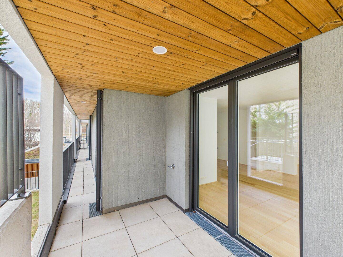 Langer, überdachter Balkon mit Fliesenboden und Holzdecke, ideal für entspannte Stunden im Freien.