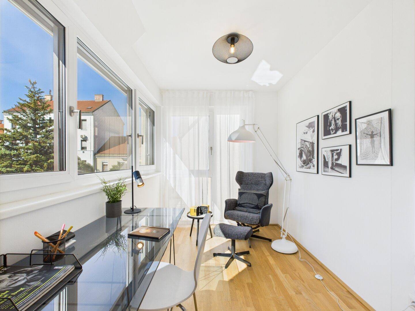 Helles Arbeitszimmer mit großem Fenster, Holzboden und modernem Schreibtisch.