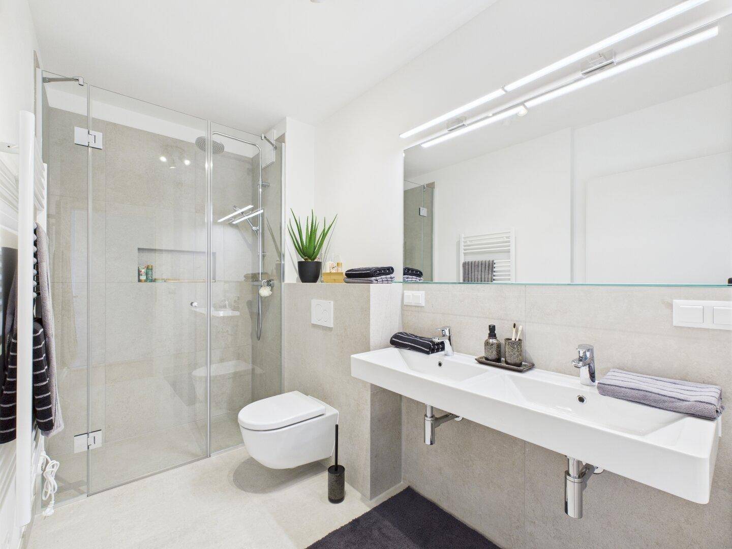 Modernes Badezimmer mit Doppelwaschbecken, großer Dusche und hellen Fliesen.