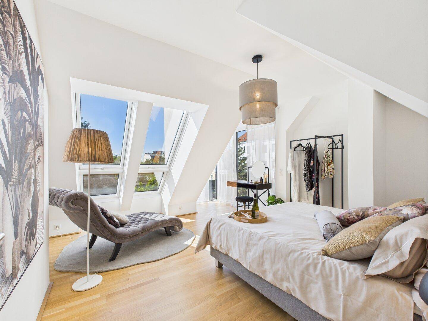 Helles Schlafzimmer im Dachgeschoss mit großen Dachfenstern, Holzboden und Liege.