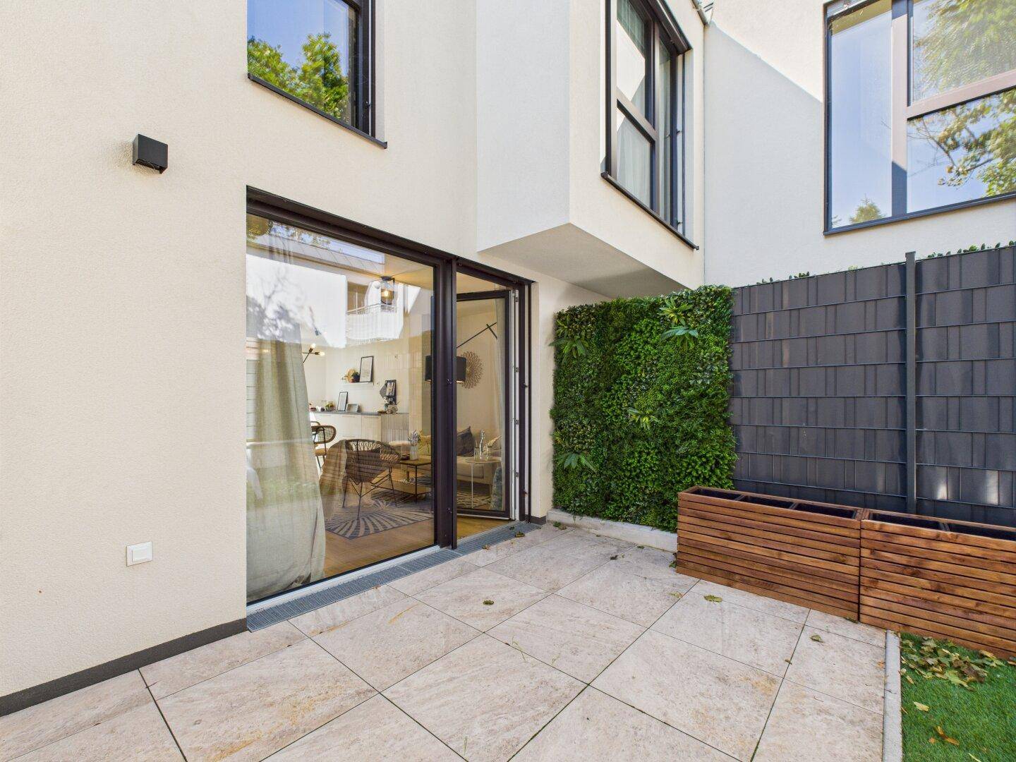 Moderne Terrasse mit Steinplatten, vertikalem Garten und Zugang zum Wohnbereich.