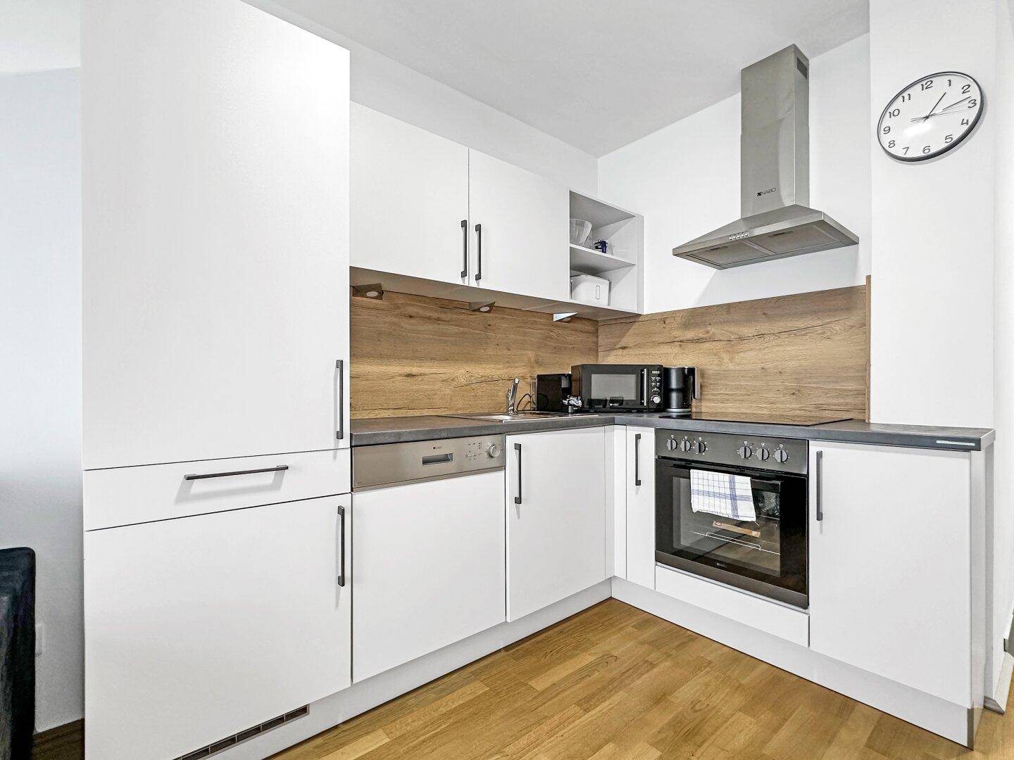 Moderne Einbauküche mit weißen Fronten, Holzrückwand und integrierten Geräten.