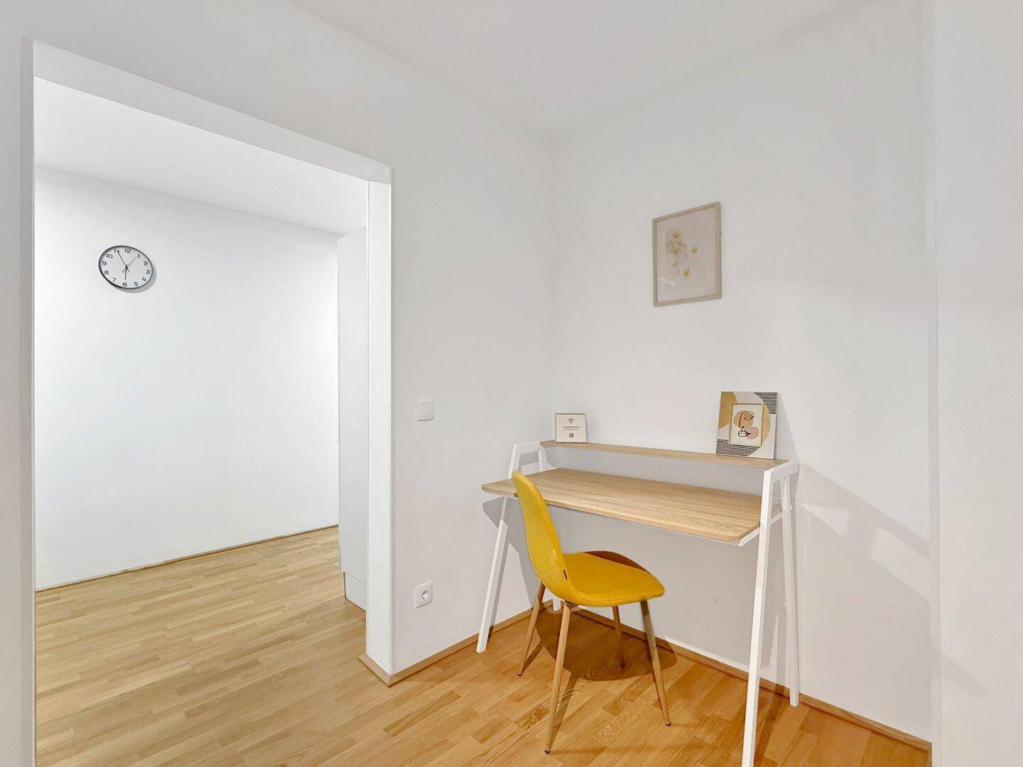 Kleiner, heller Arbeitsbereich mit Schreibtisch und gelbem Stuhl, ideal für Home-Office.