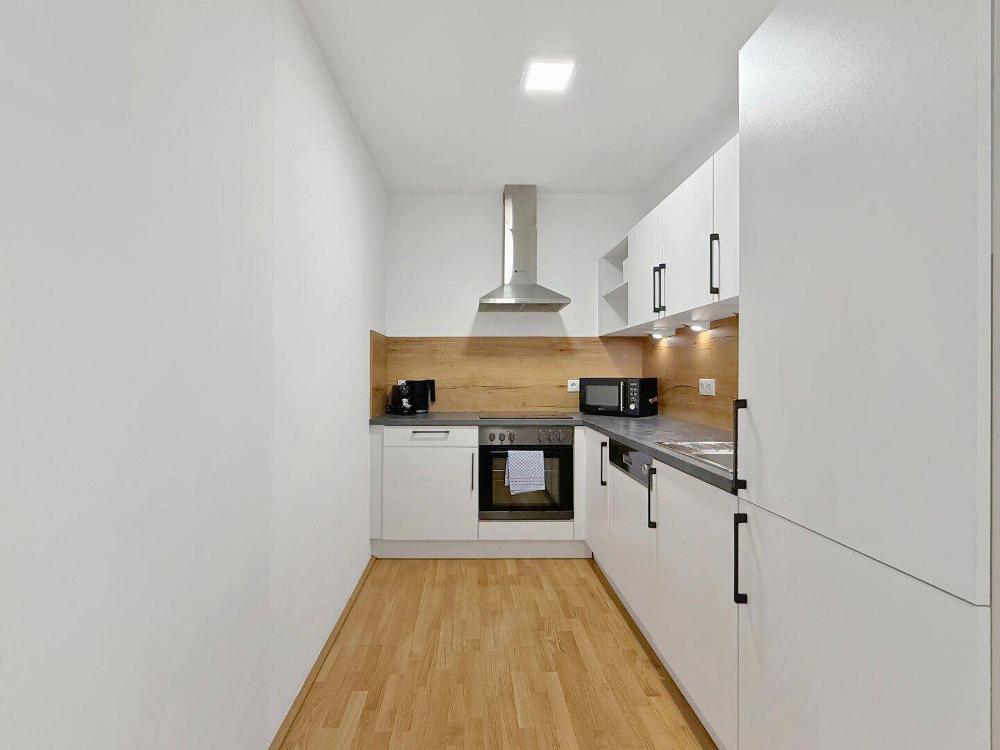 Moderne Einbauküche mit weißen Fronten, Holzrückwand und integrierten Geräten.