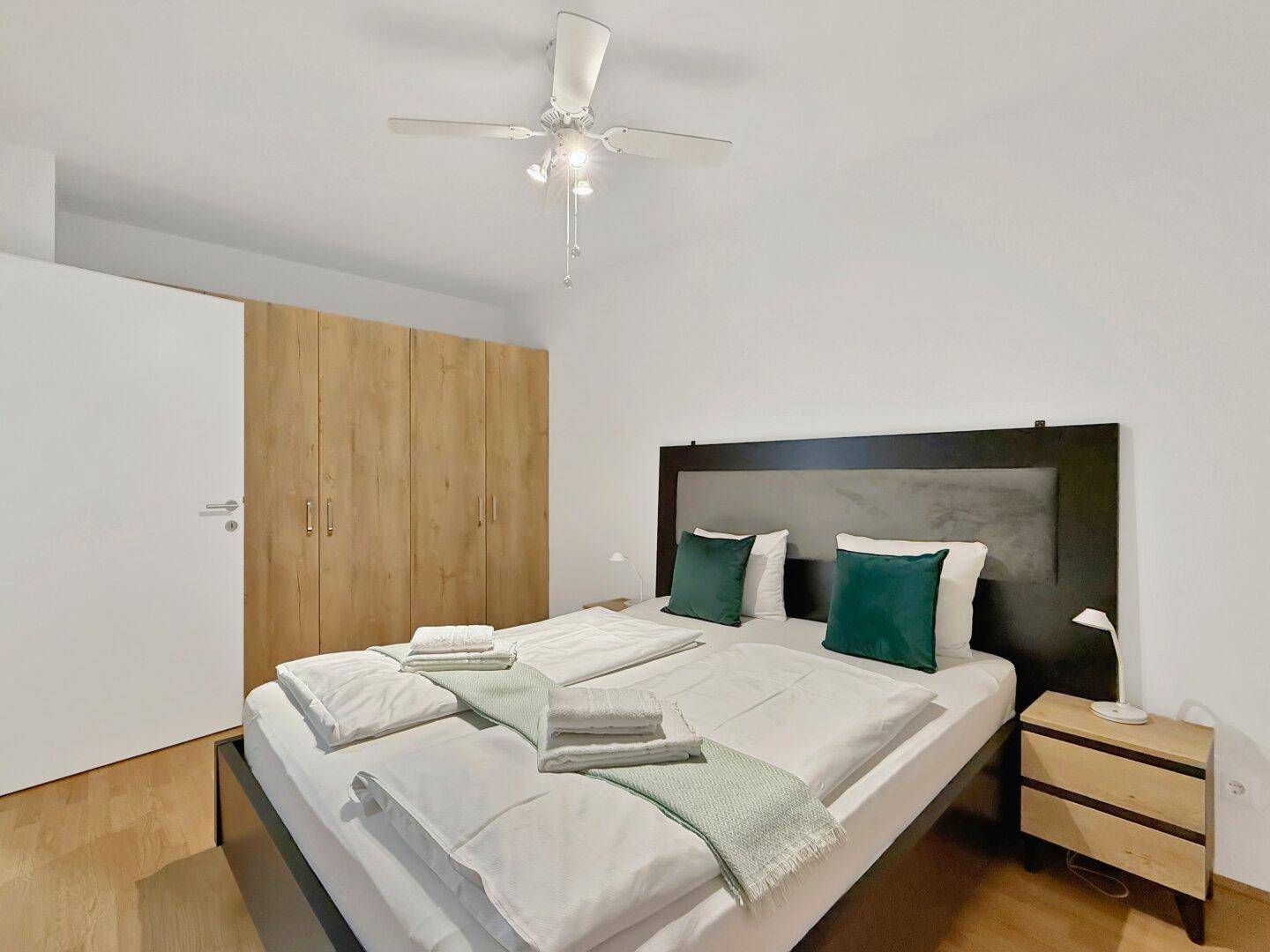 Schlafzimmer mit Doppelbett, Holzschrank und Deckenventilator für angenehmes Klima.