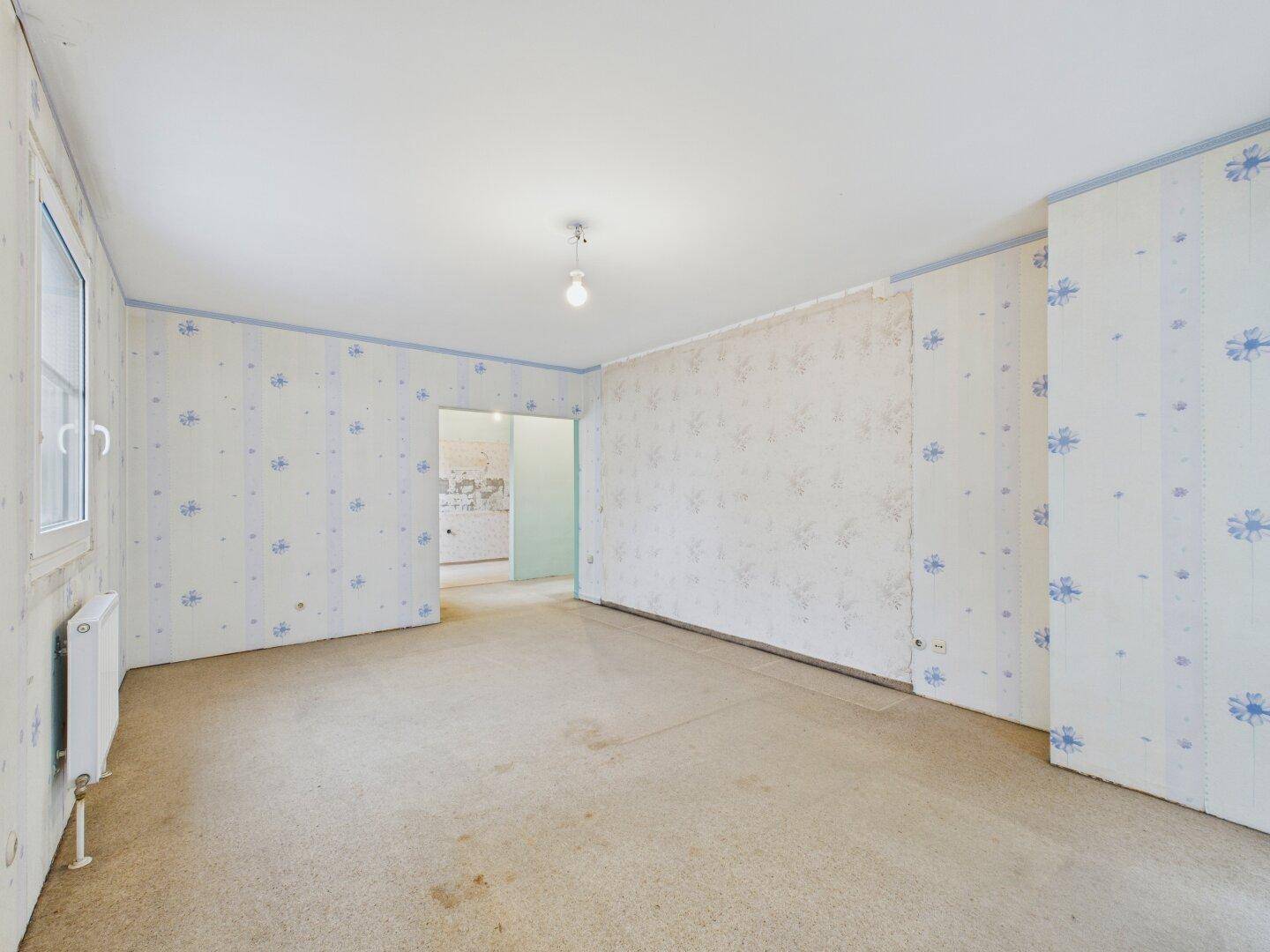 Helles Zimmer mit Teppichboden und Tapeten, bereit für eine Renovierung.