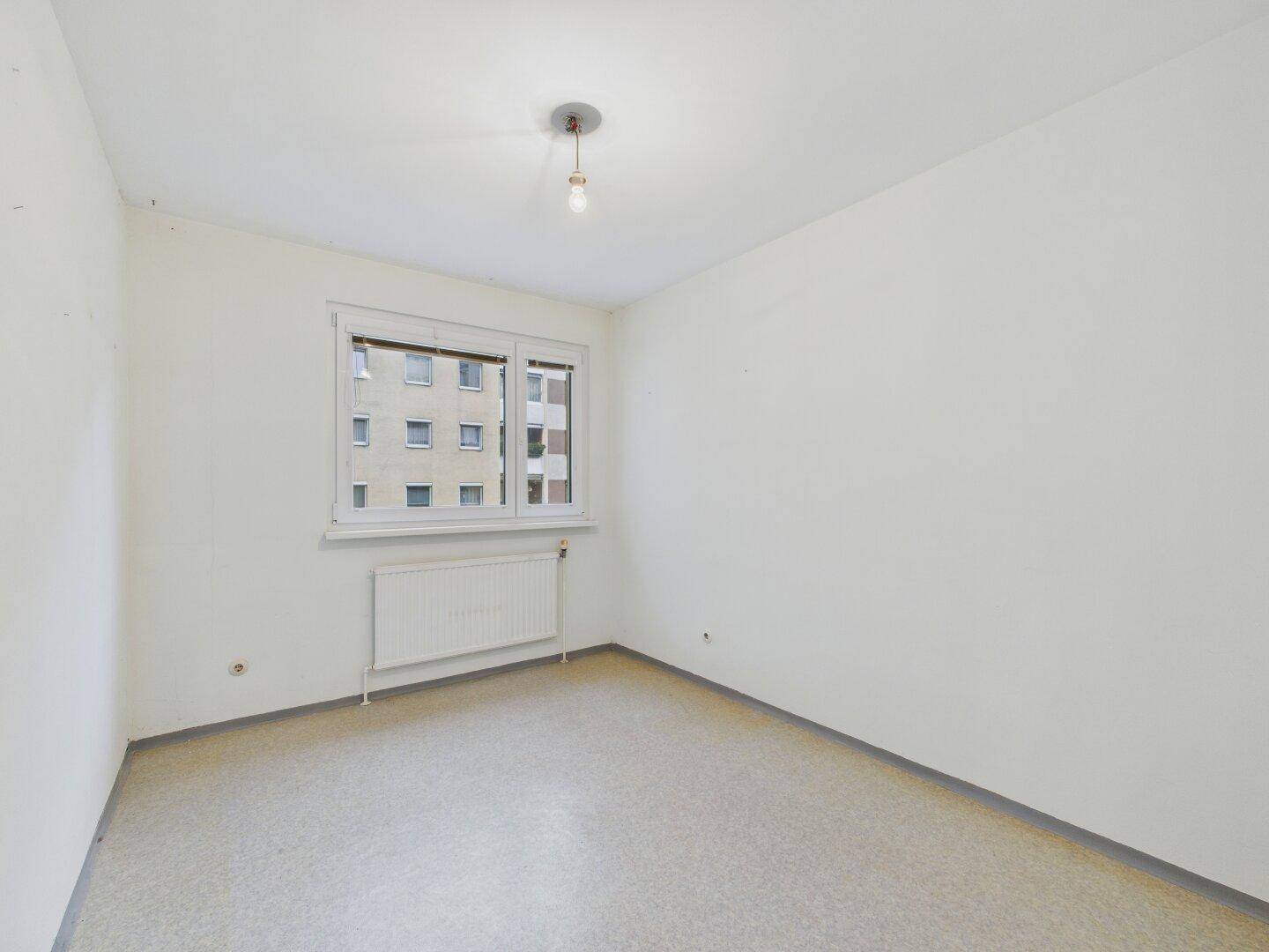 Schlichtes Zimmer mit weißen Wänden, Fenster und pflegeleichtem Bodenbelag.