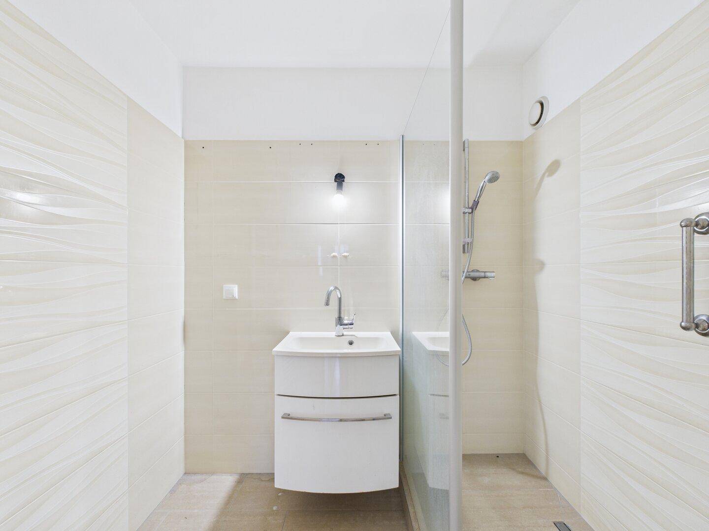 Modernes Badezimmer mit beigen Fliesen, Einzelwaschbecken und barrierefreier Dusche.