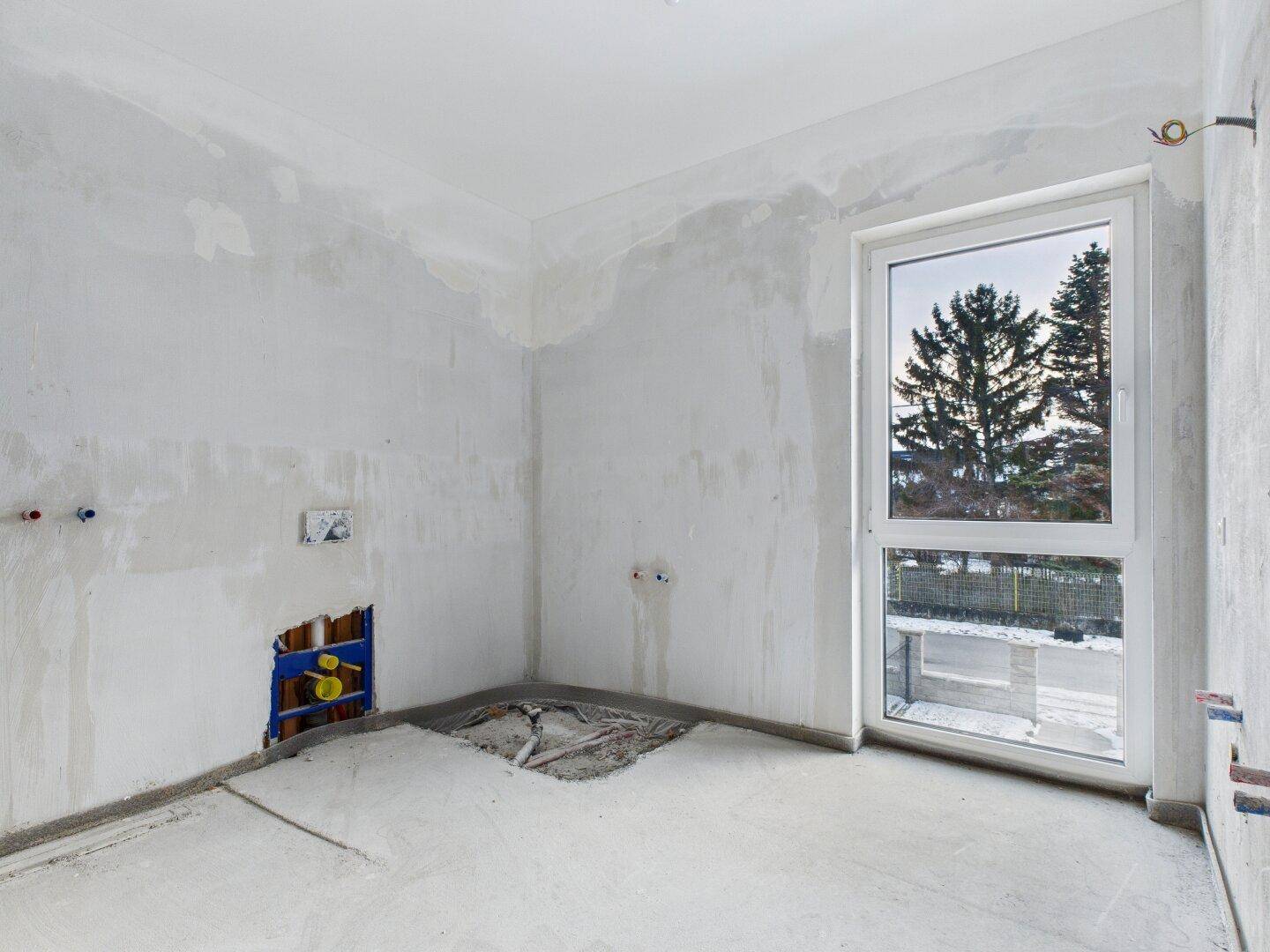 Raum im Rohbau mit sichtbaren Installationen für Wasser und Abwasser, ideal für Küche oder Bad.