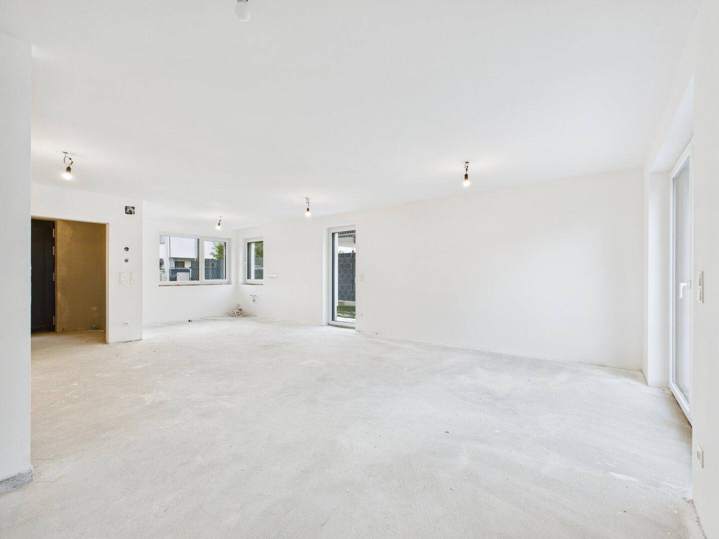 Heller, offener Raum im Rohbau mit Zugang zur Terrasse oder Garten und großen Fenstern.