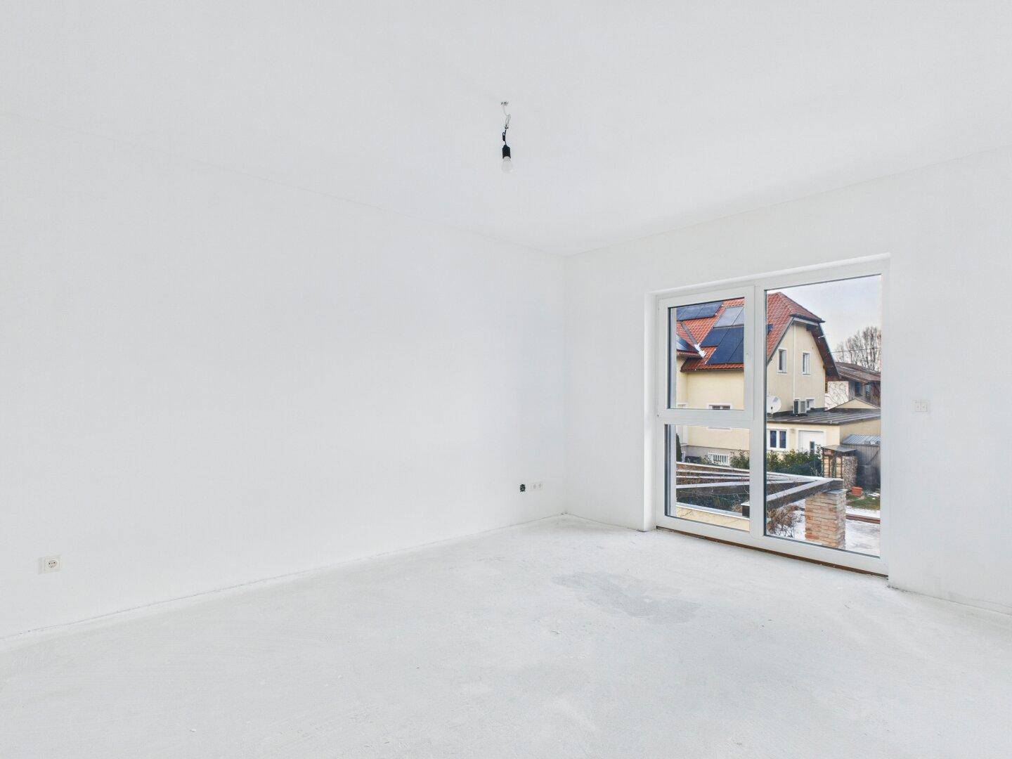 Heller Raum im Rohbau mit großem Fenster, das viel Tageslicht hereinlässt und Blick ins Grüne bietet.
