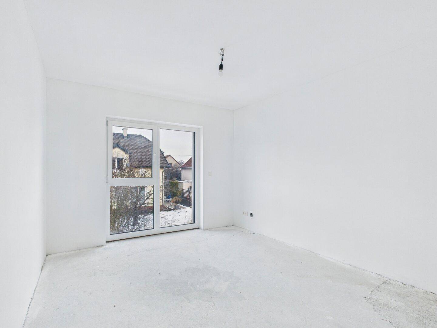 Unfertiger Raum mit großem Fenster, das viel Tageslicht hereinlässt und einen Blick auf die Nachbarschaft bietet.