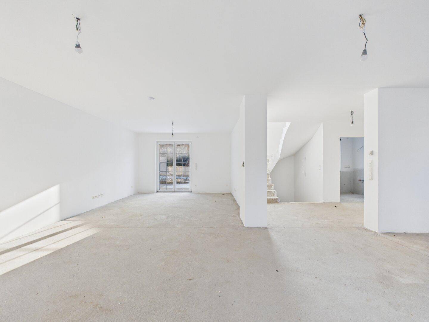 Geräumiger, unfertiger Innenraum mit Treppenaufgang und viel Tageslicht, bereit für den Ausbau.