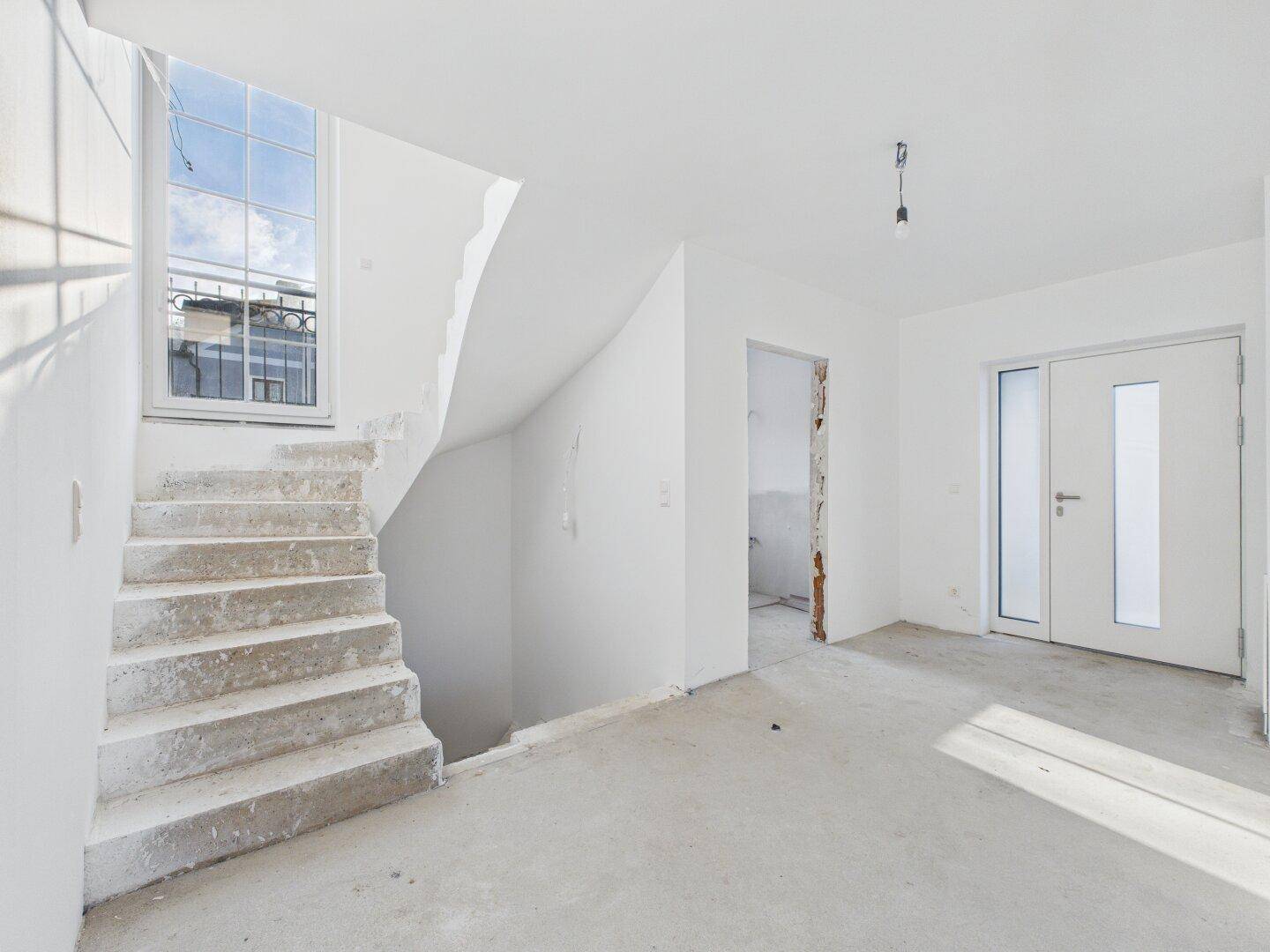 Eingangsbereich mit heller Treppe und großem Fenster, das viel Tageslicht hereinlässt.