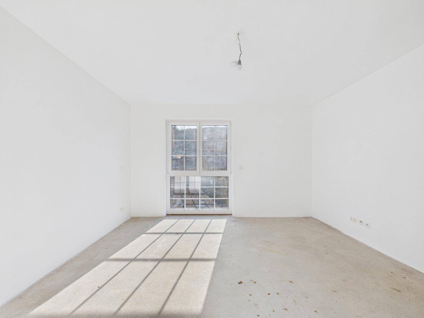 Geräumiges Zimmer im Rohbau mit großem Fenster und viel natürlichem Lichteinfall.