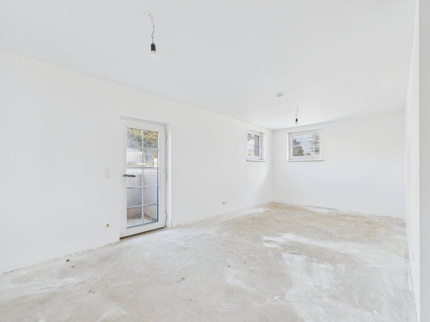 Geräumiges Zimmer im Rohbau mit viel Tageslicht und Zugang nach draußen.