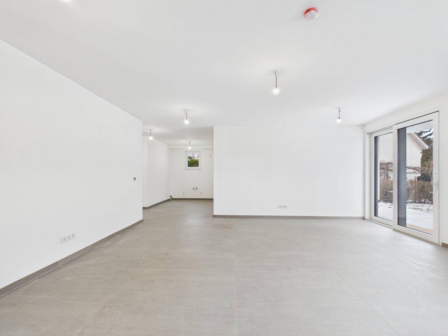 Weitläufiger Wohnbereich mit großen Fenstern und viel Tageslicht, bereit für die individuelle Einrichtung.