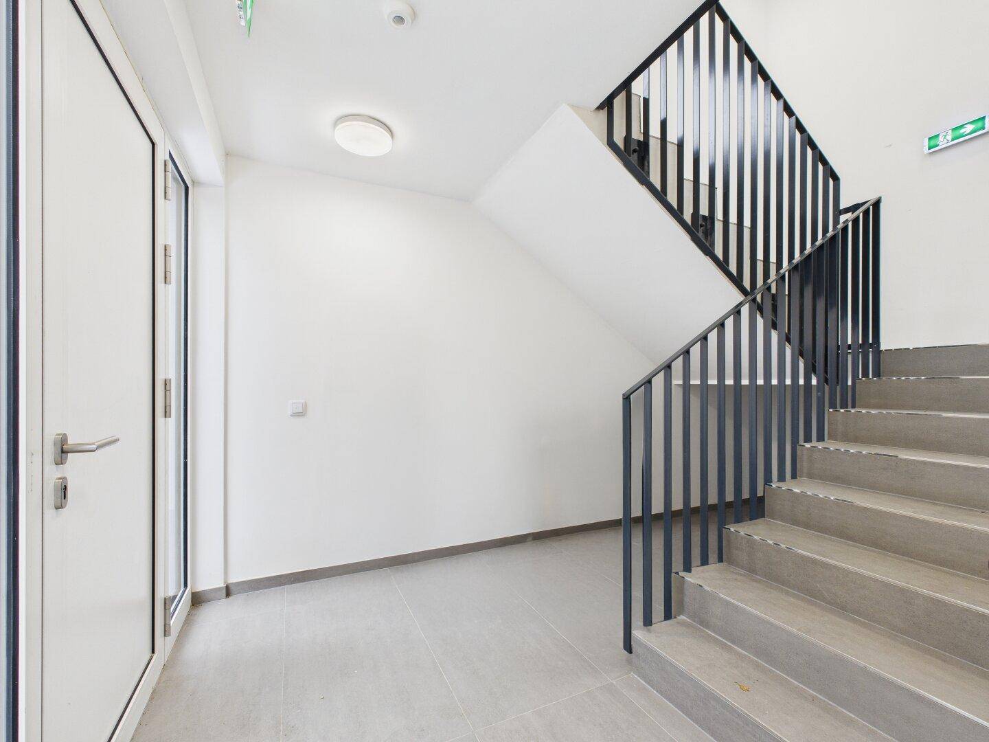 Heller Eingangsbereich mit moderner Treppe, grauen Fliesen und schlichten weißen Wänden.