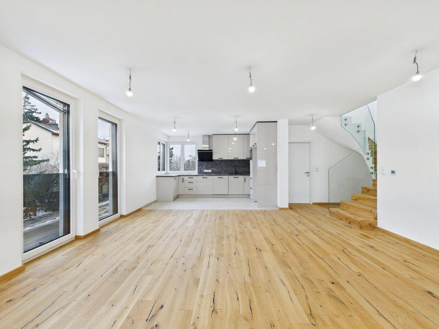 Offener Wohnbereich mit moderner Einbauküche, Holzboden und eleganter Glastreppe.