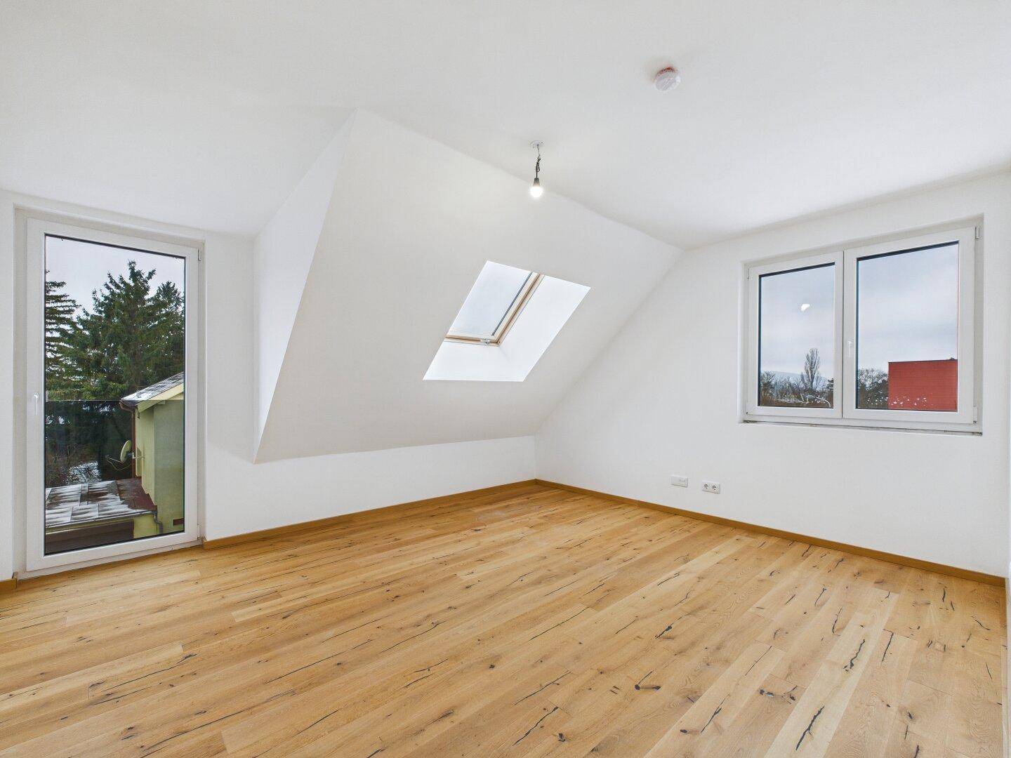 Helles Schlafzimmer im Dachgeschoss mit Holzboden, Dachfenster und Zugang zu einem kleinen Balkon.