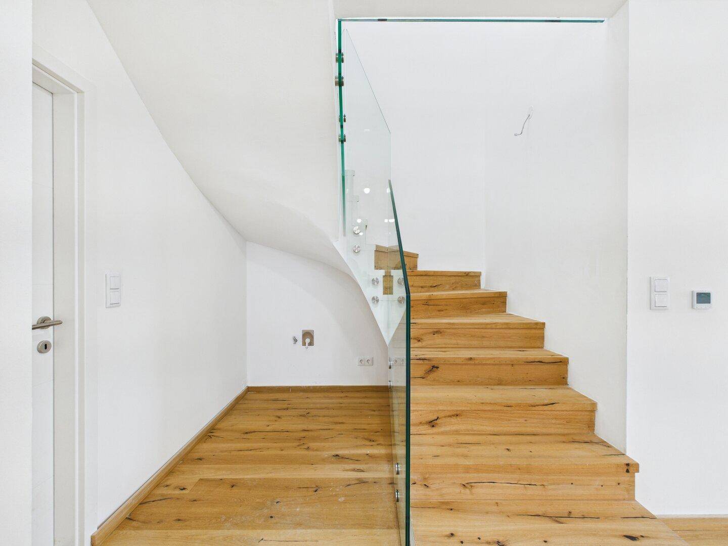 Elegante Holztreppe mit moderner Glasbrüstung, die verschiedene Ebenen des Hauses verbindet.