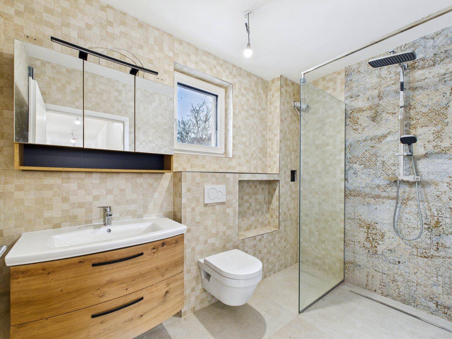 Modernes Badezimmer mit beigen Mosaikfliesen, Dusche und wandhängendem WC.