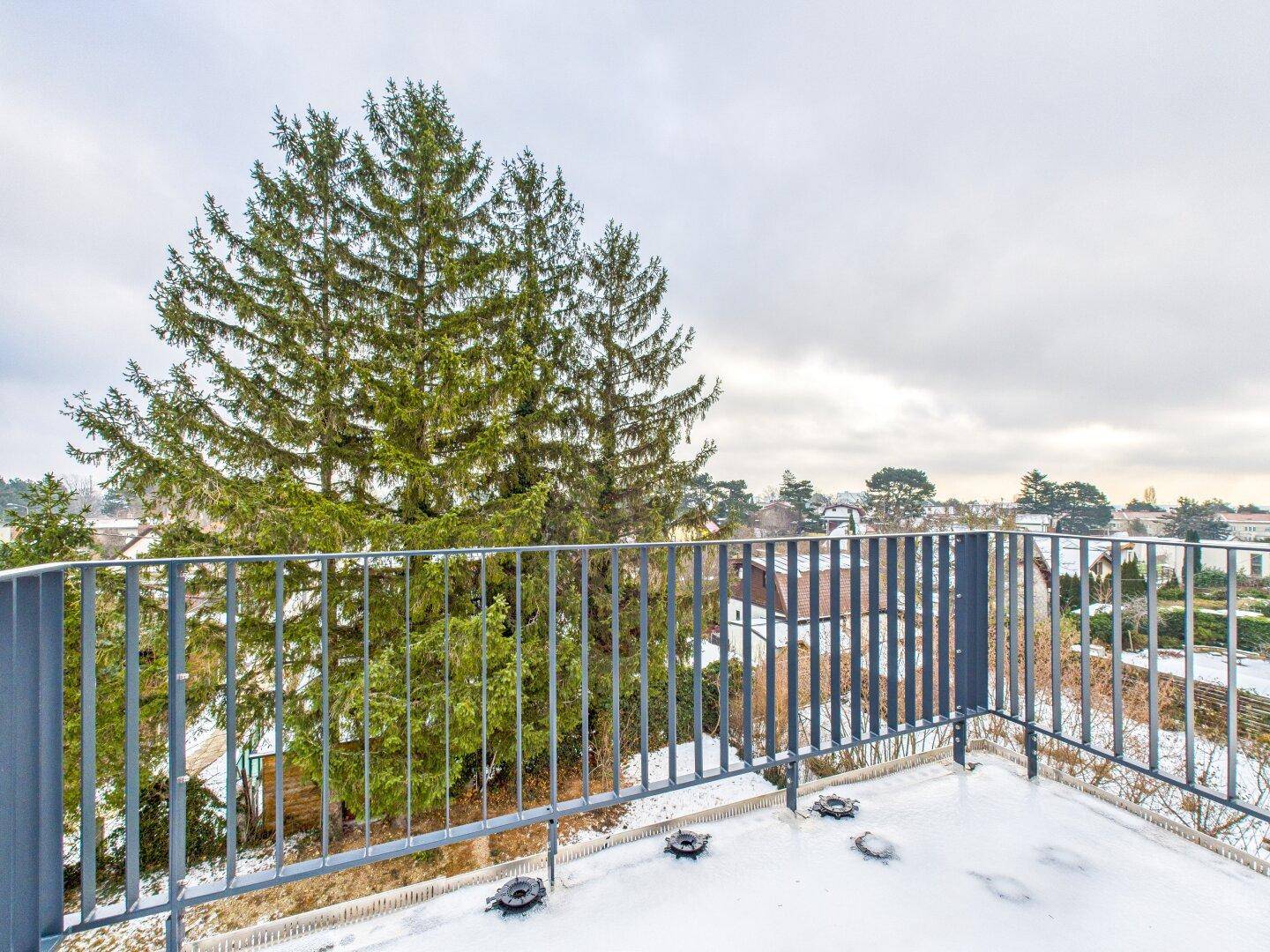 Balkon mit Metallgeländer und Blick auf die verschneite Umgebung und Bäume.
