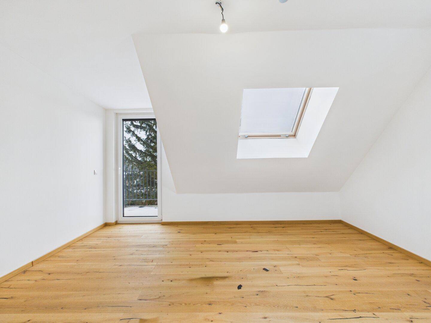 Helles Dachgeschosszimmer mit Holzboden, Dachfenster und Zugang zu einem kleinen Balkon.