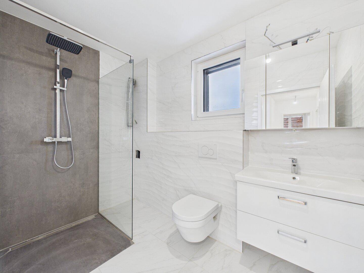 Modernes Badezimmer mit weißen Marmorfliesen, großer Dusche und wandhängendem WC.