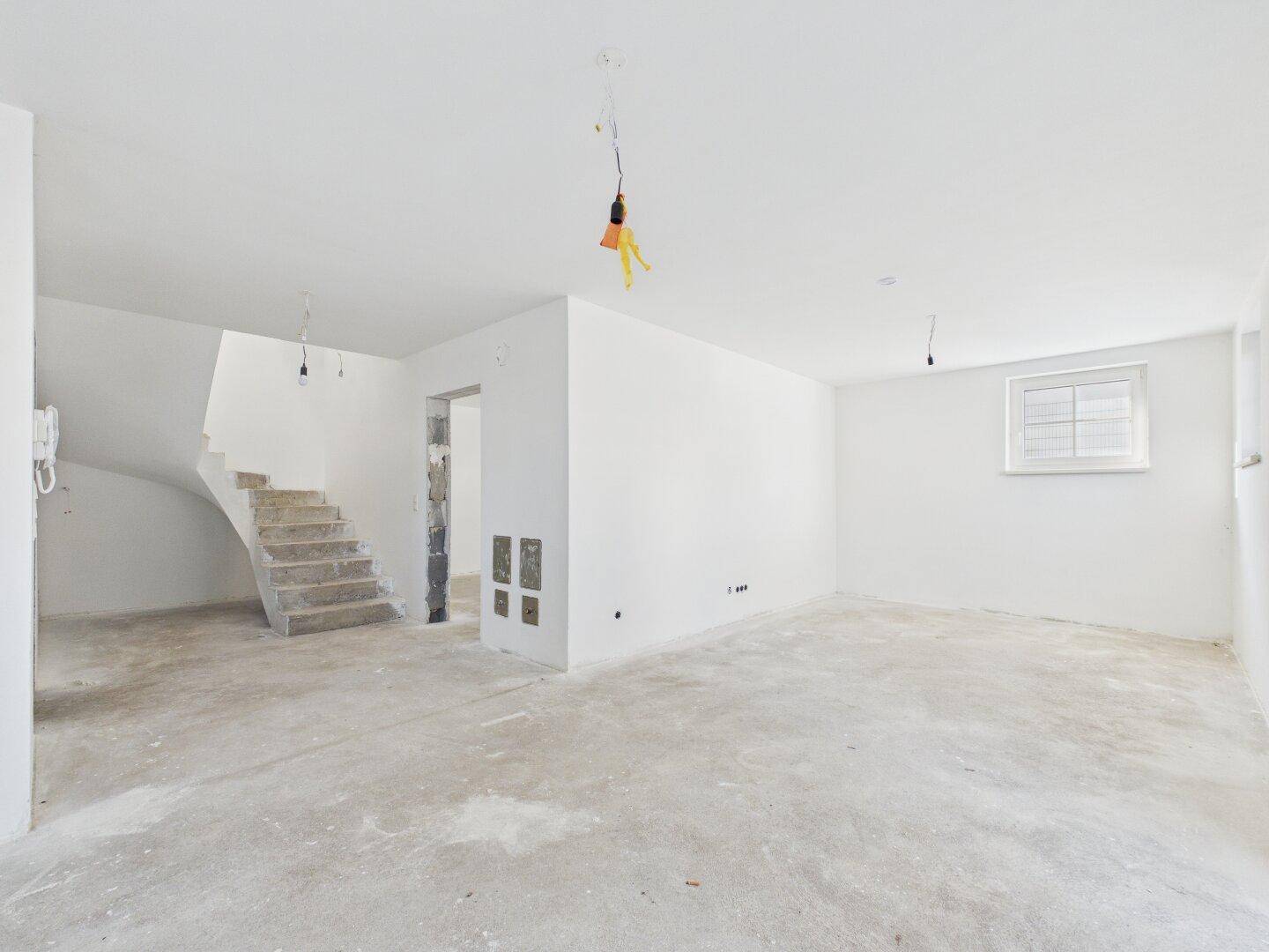 Geräumiger Wohnbereich im Rohbau mit Treppenaufgang und Fenster, ideal für offene Gestaltungskonzepte.