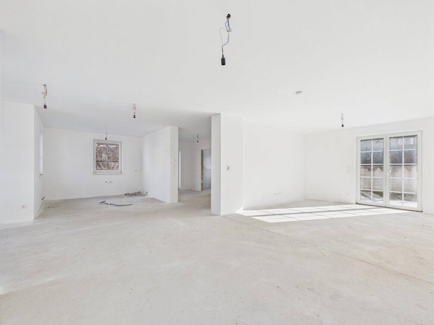 Großzügiger, heller Wohnbereich im Rohbau mit viel Tageslicht und breiter Terrassentür, ideal für offene Gestaltung.