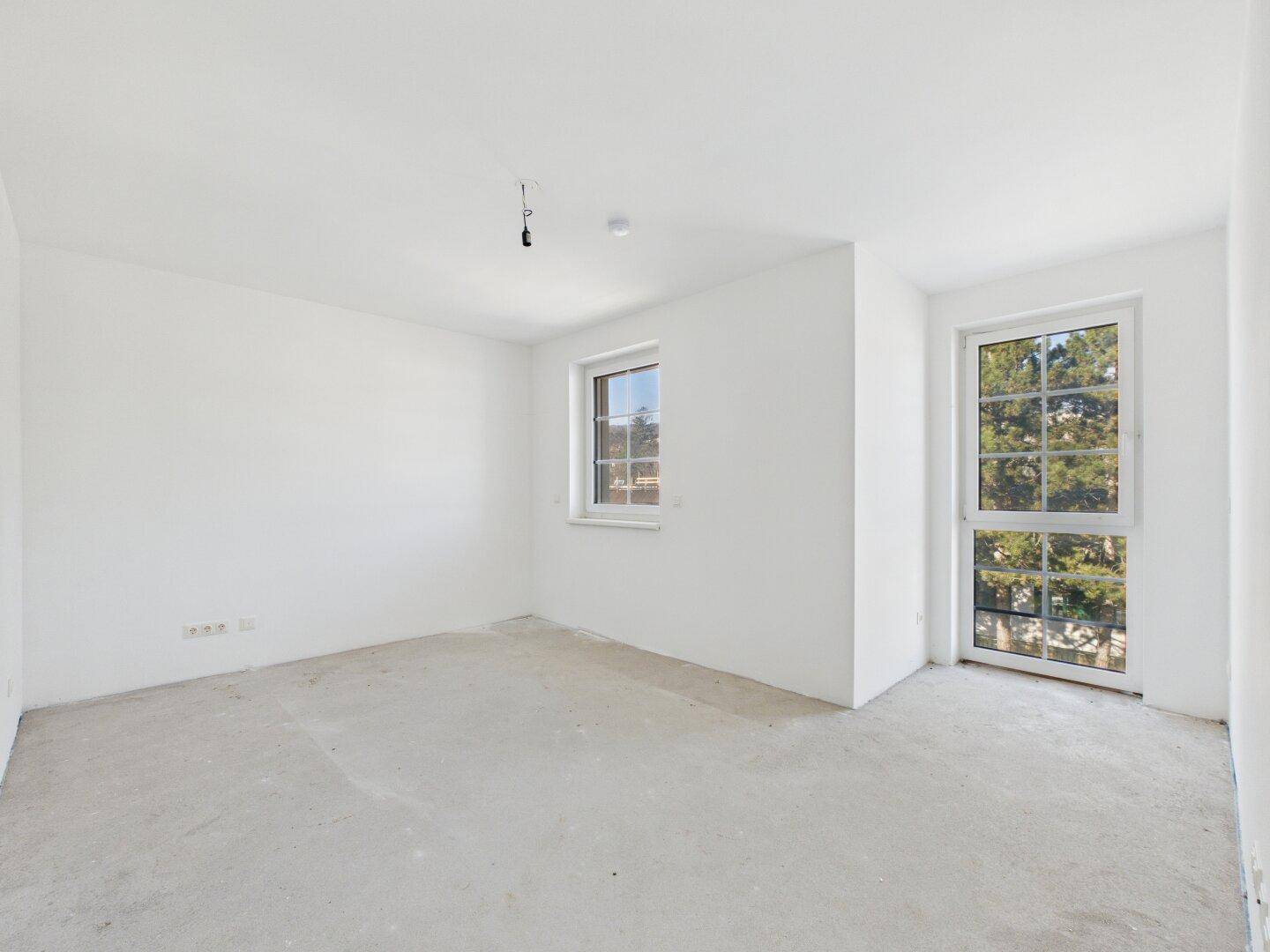 Helles Schlafzimmer im Rohbau mit Fenster und Zugang zu einem möglichen Balkon oder einer Terrasse.