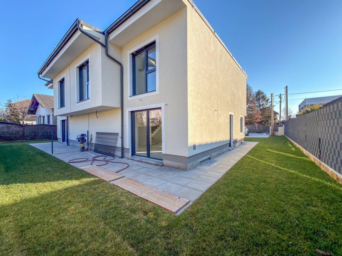 Rückseite des modernen Hauses mit großen Glasfronten, angrenzender Terrasse und weitläufigem Rasenbereich.
