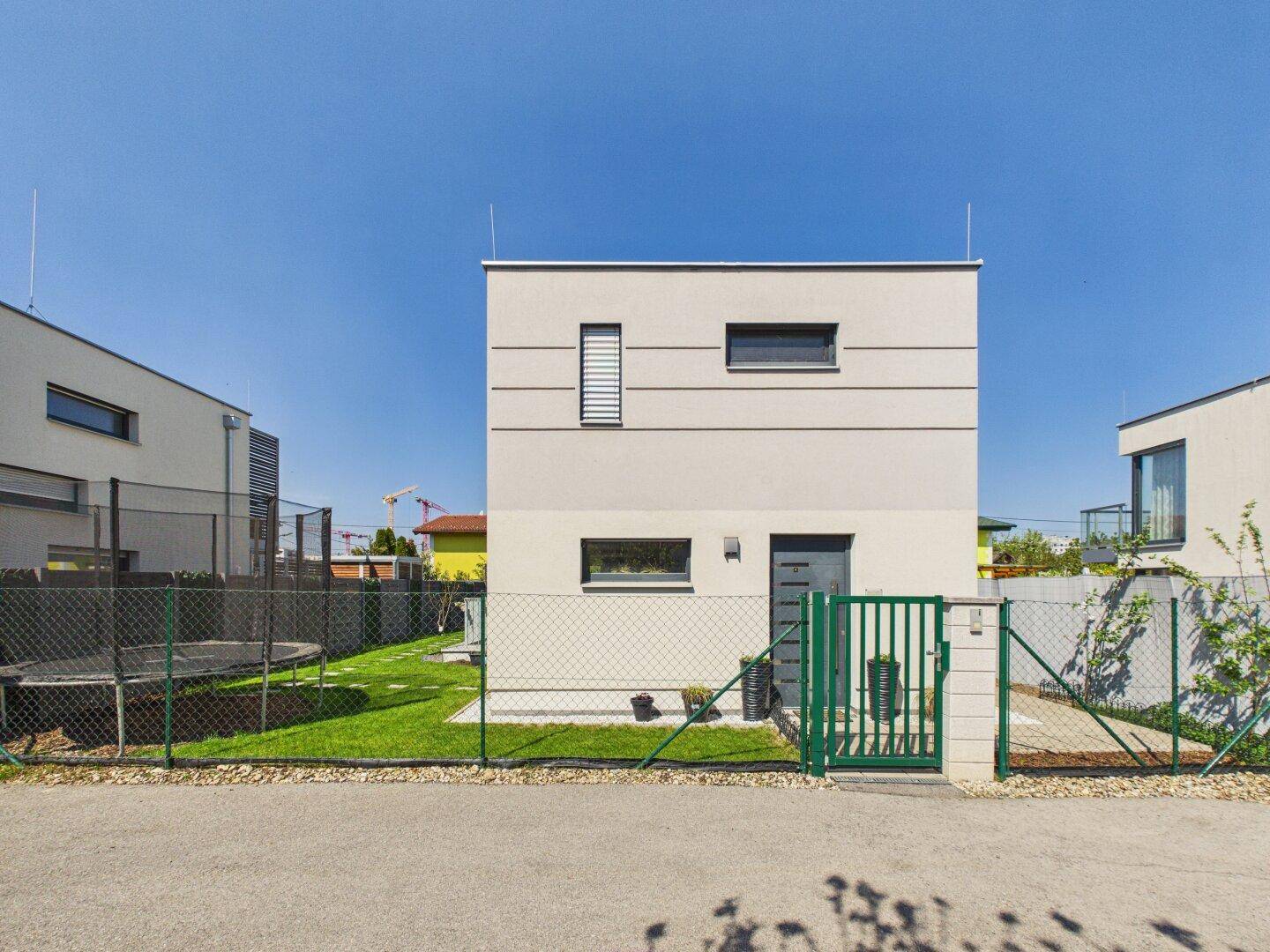 Moderne Neubaufassade mit klaren Linien, kleinen Fenstern und umzäuntem Vorgarten.