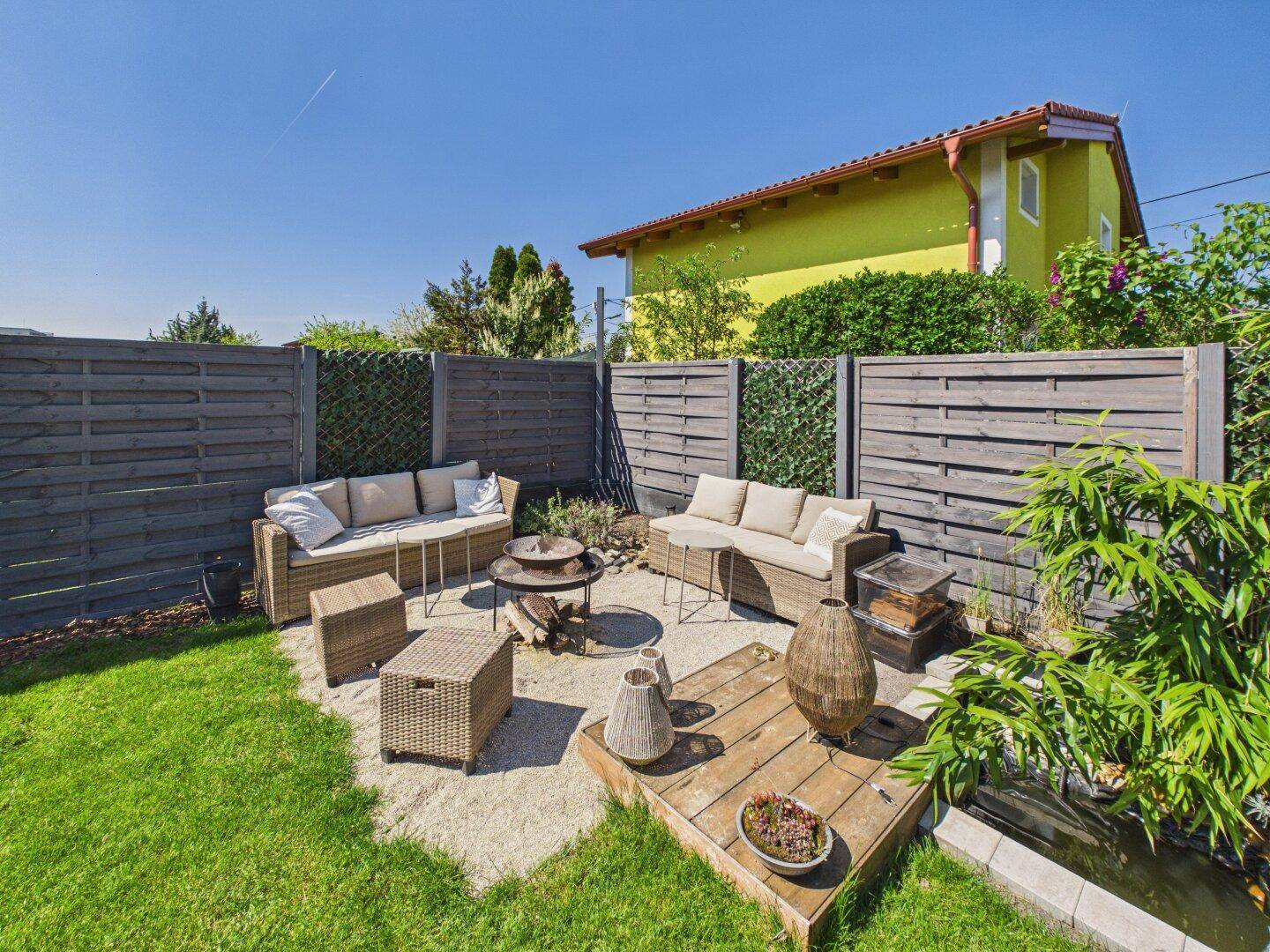 Gemütlicher Gartenbereich mit Sitzgelegenheiten, Holzzaun und kleiner Teichanlage.