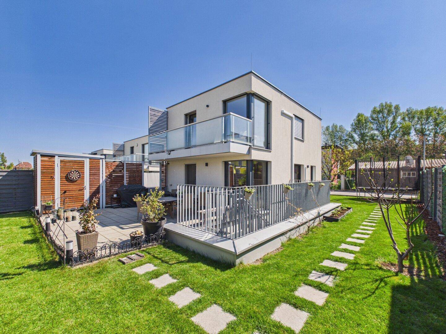 Moderner Garten mit Rasenfläche, Steinfliesenweg und großer Terrasse am Haus.
