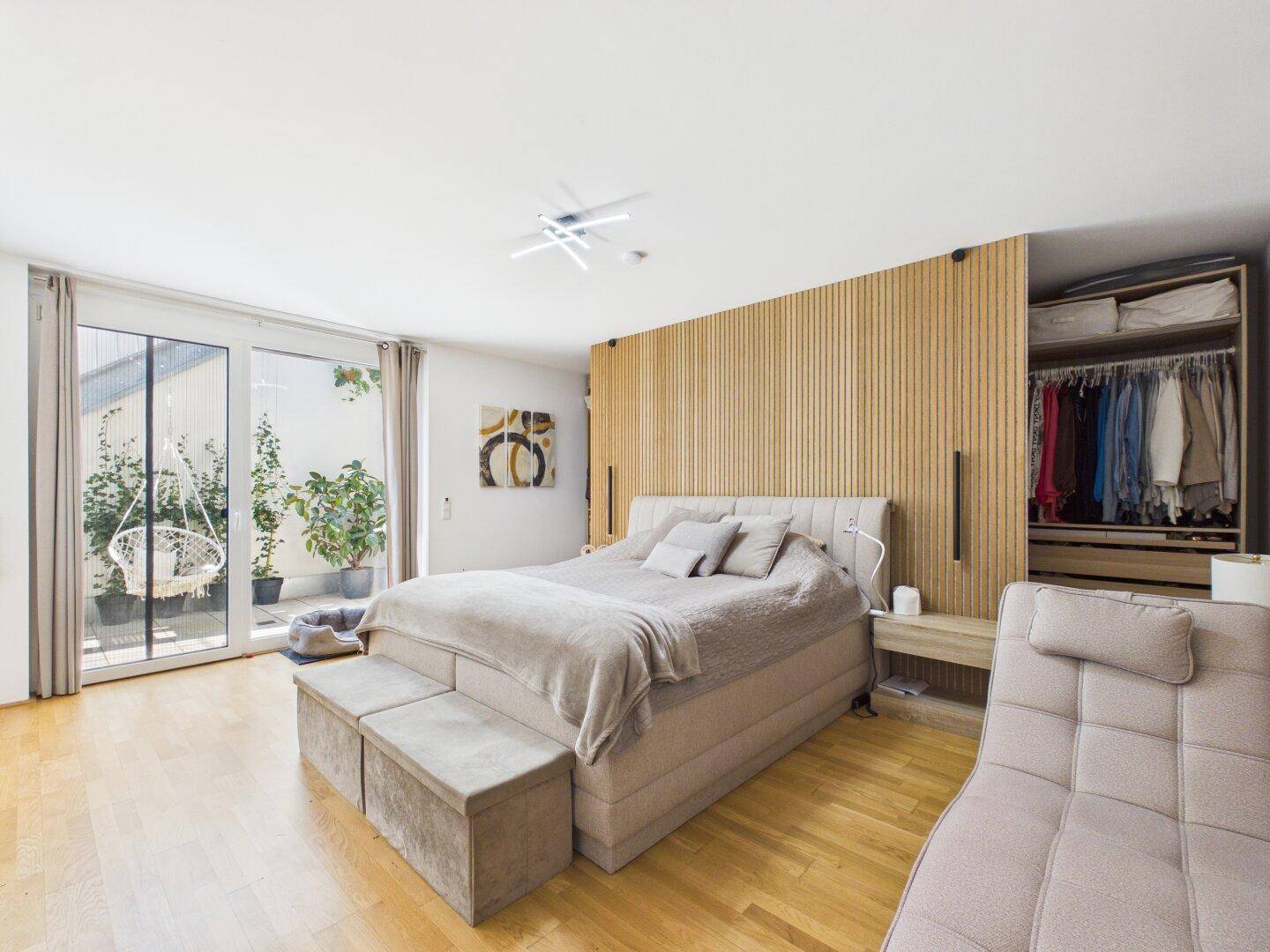 Modernes Schlafzimmer mit Holzwand, großem Bett und Zugang zu einer Terrasse.
