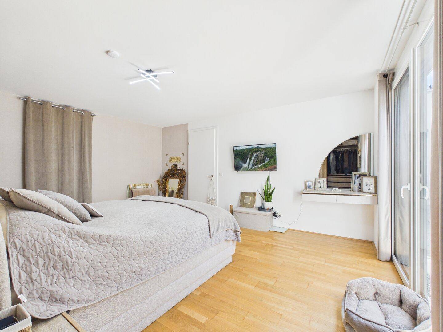 Helles Schlafzimmer mit Holzboden, großem Bett und bodentiefen Fenstern.