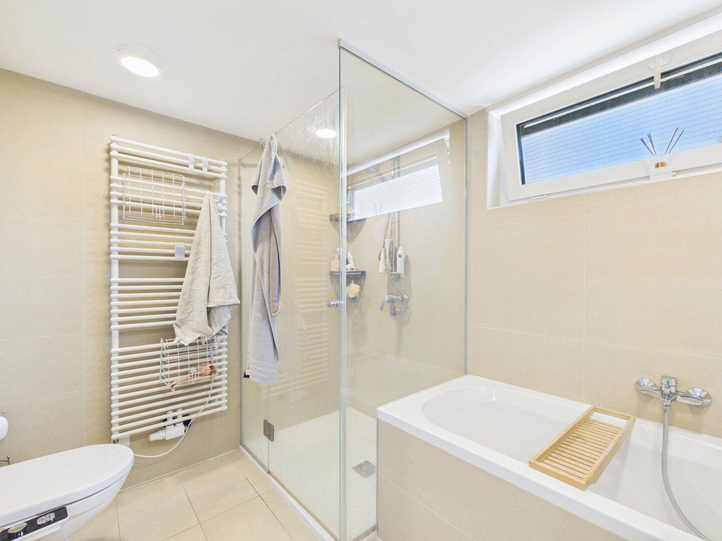 Modernes Badezimmer mit Badewanne, Duschkabine und beheiztem Handtuchhalter.
