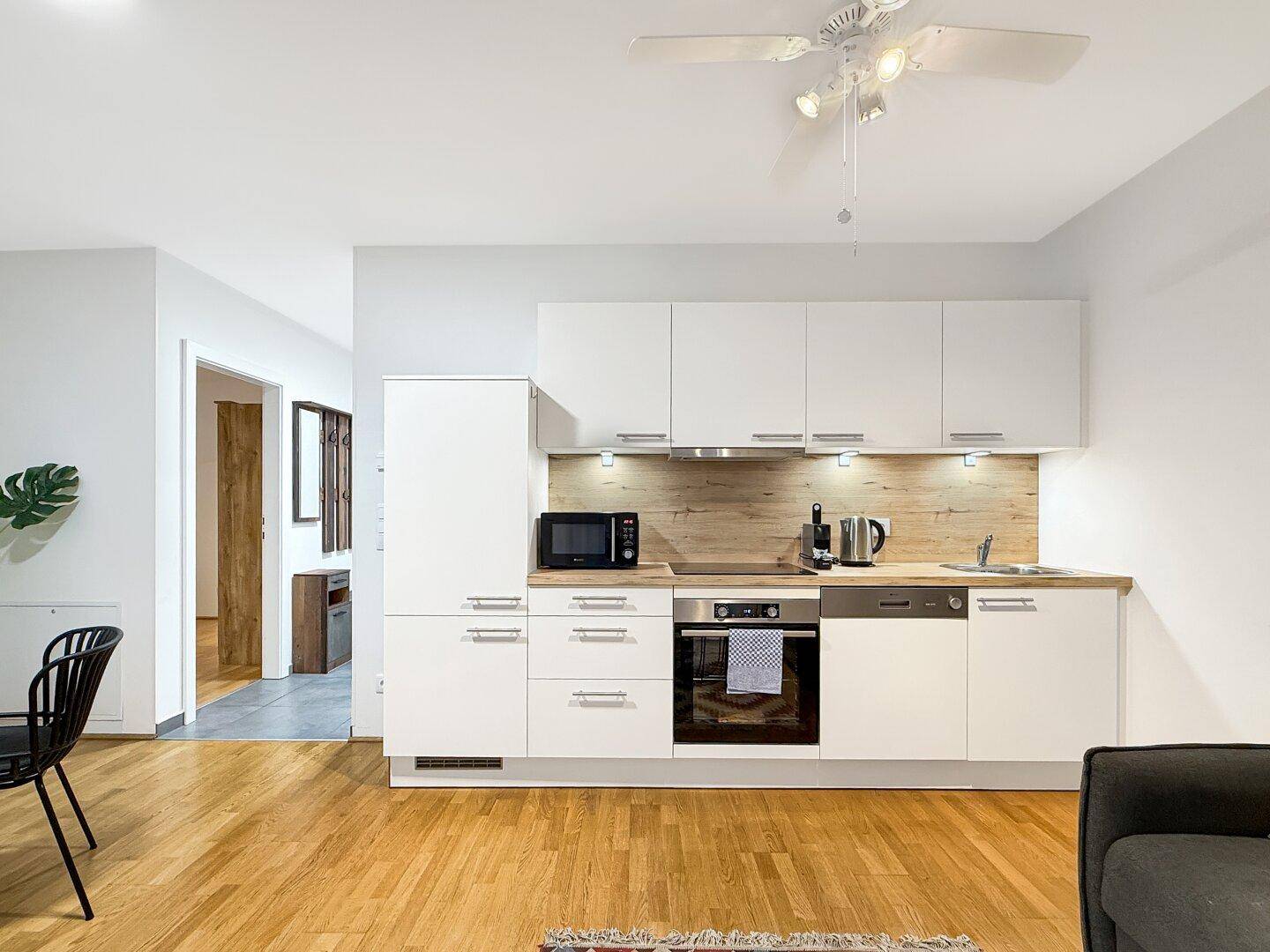Moderne Einbauküche mit weißen Schränken, Holzoptik-Arbeitsplatte und integrierten Geräten.