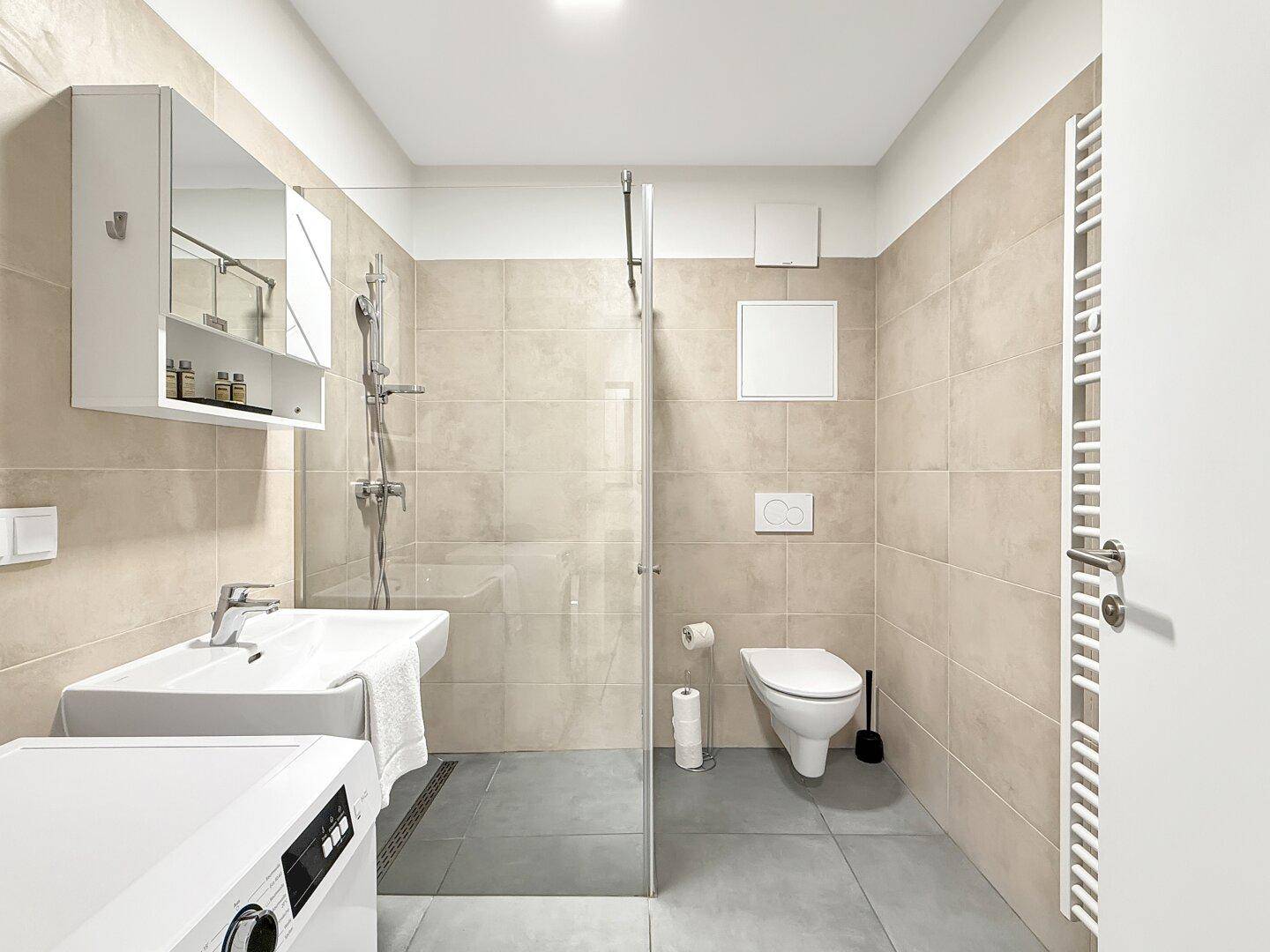 Modernes Badezimmer mit ebenerdiger Dusche, WC, Waschbecken und Waschmaschine.