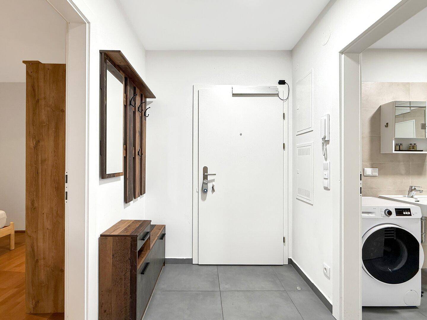 Eingangsbereich mit Garderobe, Fliesenboden und Blick auf die Waschmaschine im Bad.