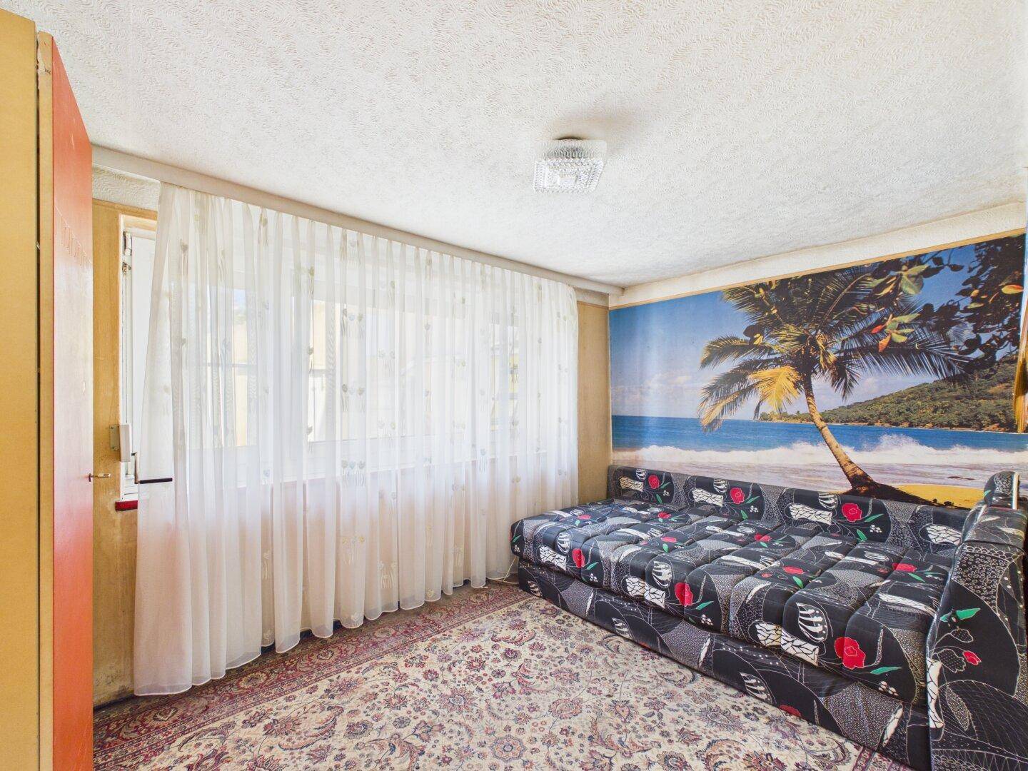 Kleines Zimmer mit Schlafsofa, Strandwandbild und gemustertem Teppichboden.
