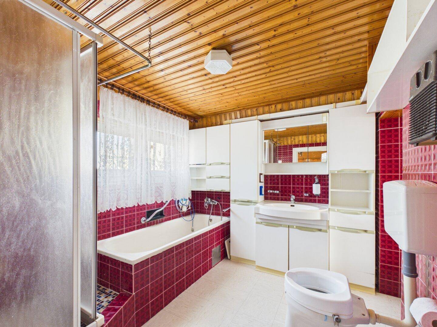 Badezimmer mit roten Fliesen, Badewanne, Duschkabine, Waschtisch und Holzdecke.